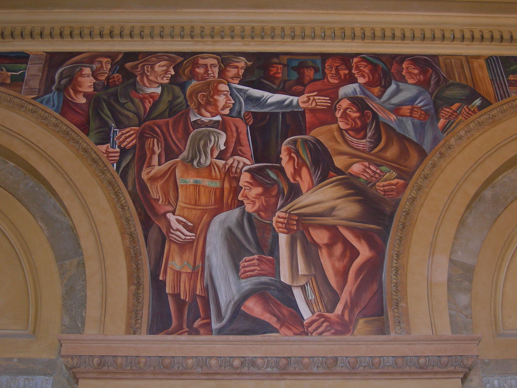 “San Antonio’s Importance In Texas history, ” Mural by Howard Norton Cook installed June 12, 1939 at the at the U.S. Main Post Office Building, now the Hipolito F. Garcia Federal Building, in downtown San Antonio.  The mural depicts Penateka leaders dressed in shawls and have long dark hair on the right side and White men on the left side with nice coats one. One of the white men is holding a gun, another is pointing at the Penateka leaders, and another is holding a blonde child in a buckskin dress.