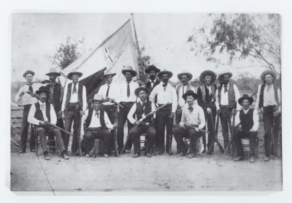 Ranger Company E, 1892. Black and white photograph of a group of white men with guns posing in front of an encampment.